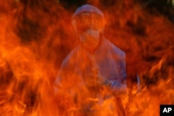A man in a protective suit stands next to the burning pyre of a person who died of COVID-19, at a crematorium in Srinagar, Indian-controlled Kashmir, May 28, 2021.