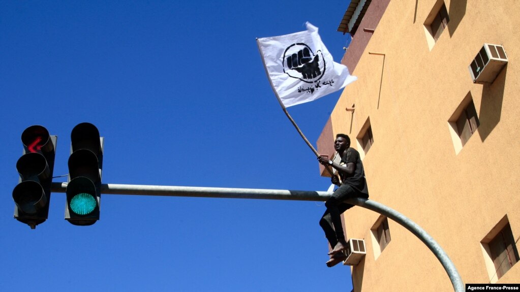 FILE - A Sudanese demonstrator sits atop a traffic light as tens of thousands protest in the capital Khartoum on Dec. 30, 2021.