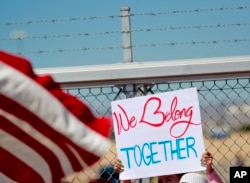 A protester holds a sign outside a closed gate at the Port of Entry facility, June 21, 2018, in Fabens, Texas, where tent shelters are being used to house separated family members.