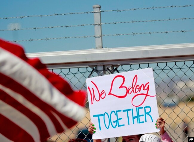 FILE - A protester holds a sign outside a closed gate at the Port of Entry facility, June 21, 2018, in Fabens, Texas, where tent shelters are being used to house separated family members.