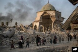 FILE - Fleeing Iraqi civilians walk past the heavily damaged al-Nuri mosque as Iraqi forces continue their advance against Islamic State militants in the Old City of Mosul, Iraq, July 4, 2017.
