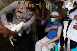 Kapolsek Galih Apria memberikan hadiah ayam kepada Jeje Jaenudin, warga Desa Sindanglaya, menerima suntikan dosis pertama vaksin COVID-19, saat program vaksinasi jemput bola di Kabupated Cianjur, Jawa Barat, Selasa, 15 Juni 2021. (Foto: Willy Kurniawan/Re