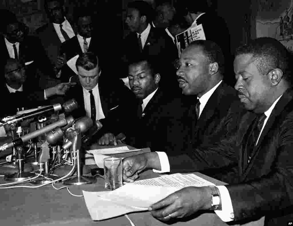 مارتین لوتر کینگ، نفر دوم از سمت راست، در کنفرانسی خبری در بالتیمور مریلند. او در کنار جان لوییس، رویس کمیته هماهنگی دانشجویی بی خشونت نشسته است. ۲ آوریل ۱۹۶۵
