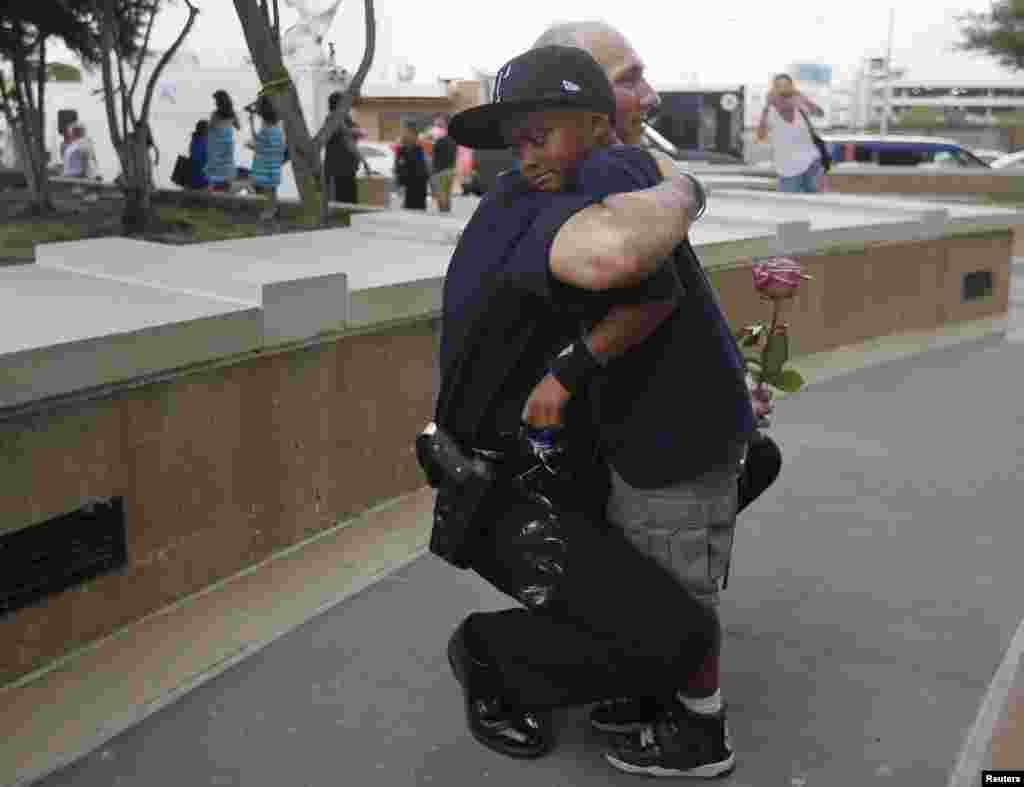 Seorang polisi memeluk seorang anak yang datang memberi penghormatan di memorial di depan kantor polisi Dallas, menyusul penembakan sejumlah polisi di kota itu (9/7). (Reuters/Carlo Allegri)