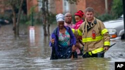 Một nhân viên thuộc Sở Cứu Hỏa St. George giúp người dân lội qua vùng nước lụt do những cơn mưa lớn gây ra trong khu chung cư Chateau Wein, Baton Rouge, La., thứ 6, ngày 12 tháng 08 năm 2016. (AP/Gerald Herbert)