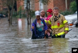 FILE - A member of the St. George Fire Department assists residents as they wade through floodwaters from heavy rains in the Chateau Wein Apartments in Baton Rouge, Louisiana, Aug. 12, 2016.