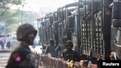 FILE - Soldiers stand next to military vehicles as people gather to protest against the military coup, in Yangon, Myanmar, Feb. 15, 2021.