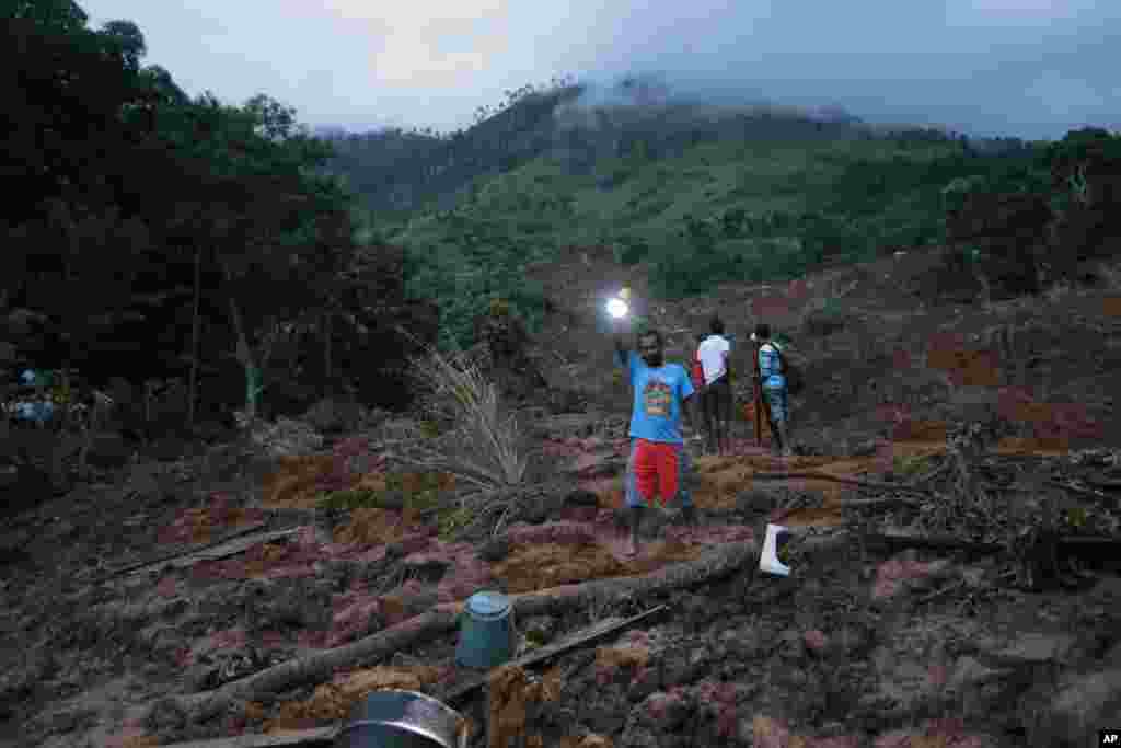 A man shines a torch as evening falls at the site of a mudslide at the Koslanda tea plantation in Badulla district, about 220 kilometers (140 miles) east of Colombo, Sri Lanka. 