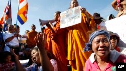 Cambodian land eviction victims and Buddhist monks shout slogans during a rally in front of the National Assembly in Phnom Penh, Cambodia, Friday, Nov. 14, 2014. They demanded to released land activists who were arrested during a protest against flooding and activists who were arrested during a protest against the jailing of land activists. (AP Photo/Heng Sinith)