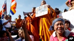 Cambodian land eviction victims and Buddhist monks shout slogans during a rally in front of the National Assembly in Phnom Penh, Cambodia, Friday, Nov. 14, 2014. They demanded to released land activists who were arrested during a protest against flooding and activists who were arrested during a protest against the jailing of land activists. (AP Photo/Heng Sinith)