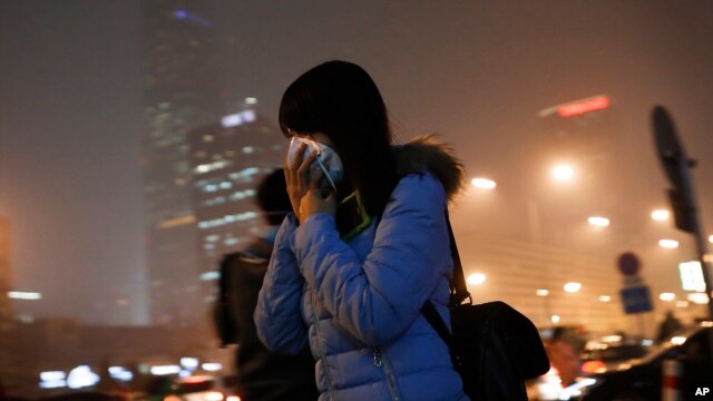 Una mujer se cubre la cara con una máscara mientras se dirige a una estación del tren subterráneo en Beijing, el martes, 8 de diciembre de 2015.

