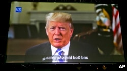 President Donald Trump is seen projected on a rear video projection screen, as he issues a welcome message for new American citizens urging them to help others assimilate and remain loyal to their new country, during naturalization ceremonies at a U.S. Citizenship and Immigration Services ceremony in Los Angeles, Sept. 20, 2017. Video projection captions reads "and God bless America." 