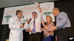 FILE - Medical student Matthew Stark, center, celebrates with his parents and Pascal J. Goldschmidt, left, dean for the University of Miami Miller School of Medicine, after learning which residency training program he was matched with, March 18, 2016, in Miami, Florida. This year, the Trump administration's travel ban, even though blocked by judges, casts a pall on prospects by foreign applicants to be allowed into the U.S., once accepted into the program.