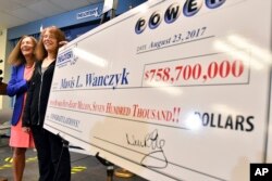 Mavis Wanczyk, of Chicopee, Mass., stands by a poster of her winnings during a news conference where she claimed the $758.7 million Powerball prize at Massachusetts State Lottery headquarters, Aug. 24, 2017, in Braintree, Mass. At left is state Treasurer Deb Goldberg.