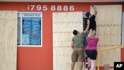 Pemasok Sekolah Cyber Christopher Rodriguez dibantu beberapa orang rekannya saat memasang panel kayu untuk menutup jendela etalase dalam persiapan Badai Irma, di Toa Baja, Puerto Rico, Selasa 5 September 2017.
