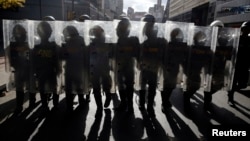 File - National Guards walk with their shields up as they keep guard during a street protest in Caracas, Feb. 18, 2015. 