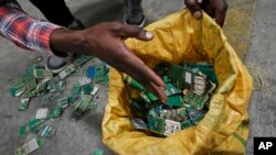 FILE - A worker gathers handfuls of cellphone printed circuit boards from a pile to put in a sack for recycling at a recycling facility near Nairobi, Kenya, in this Aug. 18, 2014 photo.