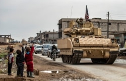 FILE - Children greet a U.S. soldier atop a Bradley Fighting Vehicle (BFV) as U.S. troops patrol in the Syrian town of al-Jawadiyah in the northeastern Hasakeh province, near the border with Turkey, Dec. 17, 2020.