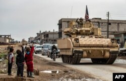 FILE - Children greet a U.S. soldier atop a Bradley Fighting Vehicle as U.S. troops patrol in the Syrian town of al-Jawadiyah in the northeastern Hasakeh province, Dec. 17, 2020.