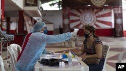 Dr. Wille Baracho takes the temperature of a woman suspected of having COVID-19 as he attends residents inside the Unidos de Padre Miguel samba school in the Vila Vintem slum of Rio de Janeiro, Brazil, May 24, 2020. (AP Photo/Lucas Dumphreys)