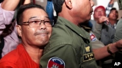 Hong Sok Hour, left, a senator from the opposition Cambodia National Rescue Party, is escorted by riot police officers, center, at Phnom Penh Municipal Court in Phnom Penh, Cambodia, Oct. 2, 2015. 