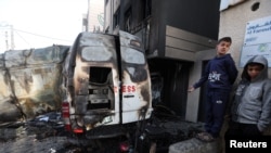 Sejumlah warga Palestina berdiri di dekat kendaraan siaran milik stasiun televisi Al-Quds Al-Youm yang terkena serangan israel di dekat Rumah Sakit Al-Awda, di Nuseirat, pada 26 Desember 2024. (Foto: Reuters/Ramadan Abed)