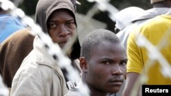 FILE - Displaced foreigners sit behind razor wire surrounding a tented refugee center in Primrose near Johannesburg, April 22, 2015