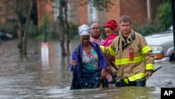 A member of the St. George Fire Department assists residents as they wade through floodwaters from heavy rains in the Chateau Wein Apartments in Baton Rouge, La., Friday, Aug. 12, 2016.