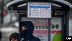 FILE - A man and a woman wearing face masks to protect against the coronavirus wait for a bus at a bus stop in central Moscow, Russia, Jan. 9, 2021. 