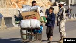 A civilian with his belongings walks past a Free Syrian Army fighter at the Syrian border crossing of Bab al-Hawa, at the Syrian-Turkish border, Oct. 22, 2013.