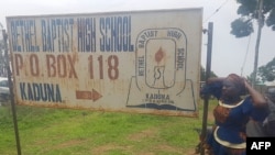 Parents stand beside signpost of Bethel Baptist School where 140 boarding students were kidnapped in Kaduna, northwestern Nigeria, July 5, 2021.