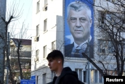 A man walks near a banner displaying former Kosovo President Hashim Thaci, in Pristina, Kosovo, March 30, 2023.