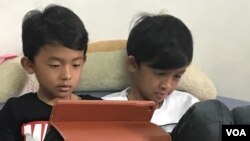 Putra ketiga dan keempat Kem Ley, Keo Veasna Mano dan Kem Veasna, sedang menonton Ipad saat VOA mewawancarai ibu mereka di tempat penampungan sementara, 2 Juli. 2017. (Sok Khemara / VOA).