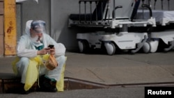 A healthcare worker sits on the curb as he uses a vaping device while taking a break outside. 