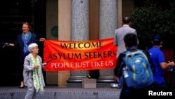 Para pejalan kaki melintas di depan pembela para pengungsi yang membentangkan spanduk di depan Gedung Custom House di pusat bisnis di Sydney, Australia, 8 Maret 2017.
