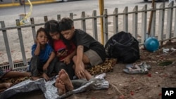 ARCHIVO - Los niños Bolaños (de izq a der) Sebastián, Kamila y Miguel Ángel, de Venezuela, miran un teléfono móvil afuera de la terminal de autobuses donde viven con su madre Keilly y otro hermano, junto con otros migrantes en Villahermosa, México, el 8 de junio de 2024. 