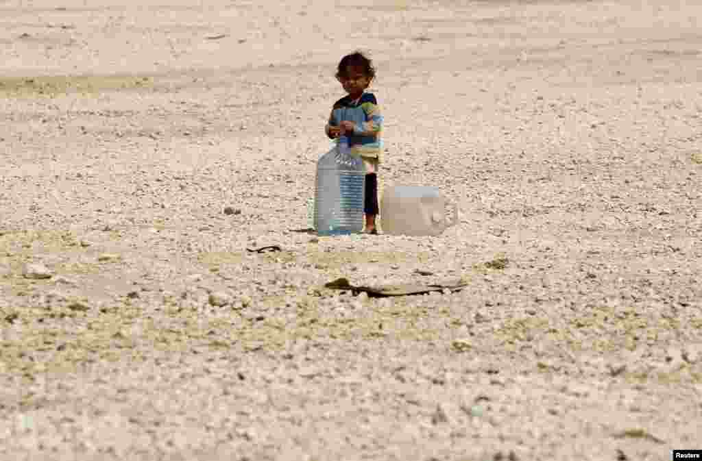 A young Syrian refugee stands beside water containers at Al-Zaatri refugee camp in the Jordanian city of Mafraq, near the border with Syria, Sept. 1, 2013. 