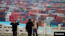 FILE - Security guards walk in front of containers at the Yangshan Deep Water Port in Shanghai, China, April 24, 2018. The U.S. will impose tariffs Friday on $34 billion worth of Chinese imports.