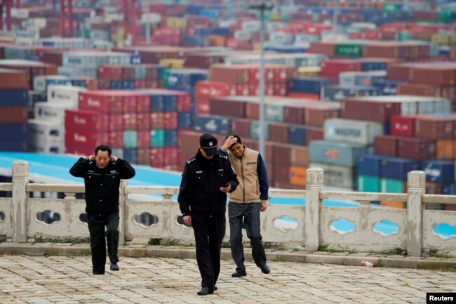 FILE - Security guards walk in front of containers at the Yangshan Deep Water Port in Shanghai, China, April 24, 2018.