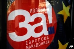 A man is reflected on a banner that reads ''For European Macedonia" in Skopje, Macedonia, Oct. 1, 2018.