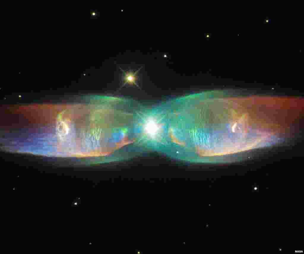 The shimmering colors visible in this NASA/ESA Hubble Space Telescope image show off the remarkable complexity of the Twin Jet Nebula. The new image highlights the nebula&rsquo;s shells and its knots of expanding gas in striking detail. Two iridescent lobes of material stretch outwards from a central star system. Within these lobes two huge jets of gas are streaming from the star system at speeds in excess of one million kilometers (621,400 miles) per hour.