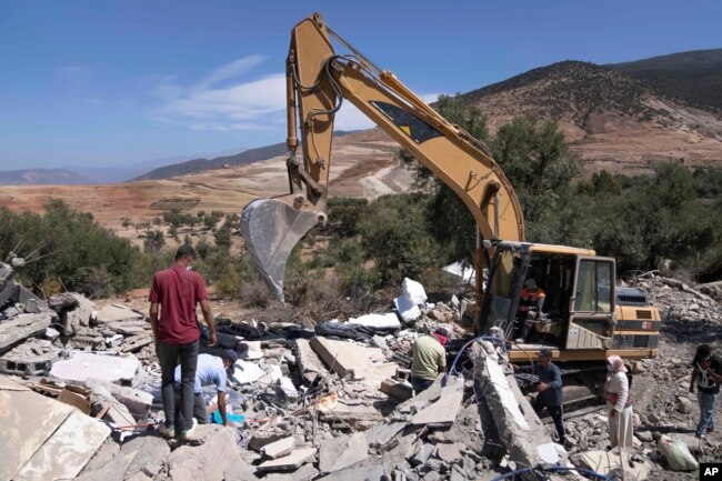 A tractor removes rubble as people search for their belongings in their home which was damaged by the earthquake, in the village of Tafeghaghte, near Marrakech, Morocco, Monday, Sept. 11, 2023. (AP Photo/Mosa'ab Elshamy)