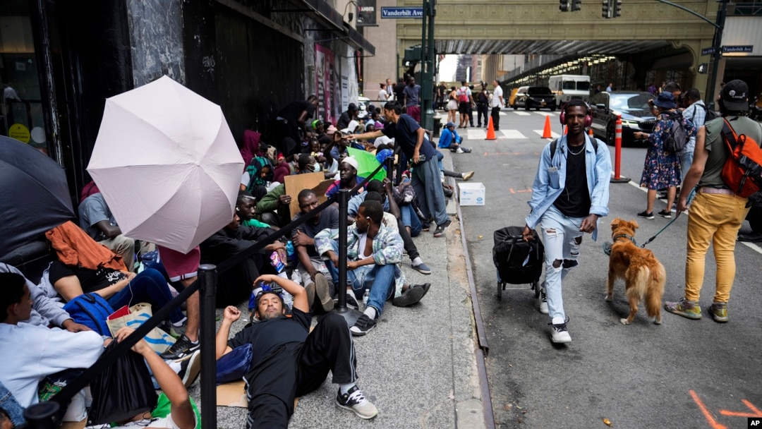 ARCHIVO - Migrantes se sientan en una fila afuera del Hotel Roosevelt, que está siendo utilizado por la ciudad como alojamiento temporal, el 31 de julio de 2023, en Nueva York.