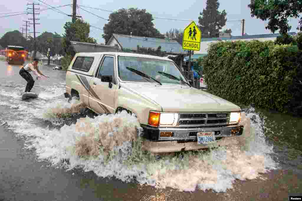 Max Barnett is pulled on a surfboard by driver Riley Johnson down a flooded street after the threat of mudslides prompted evacuation orders in east Santa Barbara, January 9, 2023.