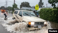 Max Barnett, 23, is pulled on a surfboard by driver Riley Johnson, 23, down a flooded street after the threat of mudslides prompted evacuation orders in east Santa Barbara, California, Jan. 9, 2023.