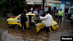 Beberapa orang mencoba mendorong taksi yang hanyut oleh banjir yang disebabkan badai tropis Amanda di kawasan El Modelo, di San Salvador, El Salvador, 31 Mei 2020. 