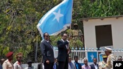 Le nouveau président somalien Mohamed Abdullahi Farmajo brandit le drapeau de la Somalie au cours de la cérémonie de la passation de pouvoir avec le président sortant du pays Hassan Sheikh Mohamud, au centre à gauche, à Mogadiscio, Somalie, 16 février 2017.