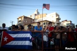 A man holds a U.S. flag while gathering with others on a sidewalk near the U.S. embassy (not pictured) in Havana, Cuba, Aug. 14, 2015.