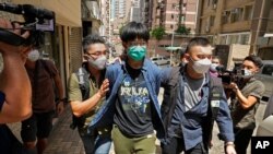 A student of Hong Kong University, center, with green mask, is escorted by police officers in Hong Kong, Aug. 18, 2021. The student and three other Hong Kong university students were arrested Wednesday on accusations of advocating terrorism.