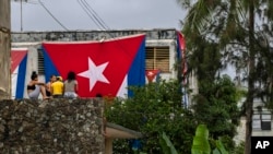 Neighbors look at Cuban flags draped over the windows of opposition activist Yunior Garcia Aguilera's home, in an attempt to stop him from communicating with the outside in Havana, Cuba, Nov. 14, 2021.